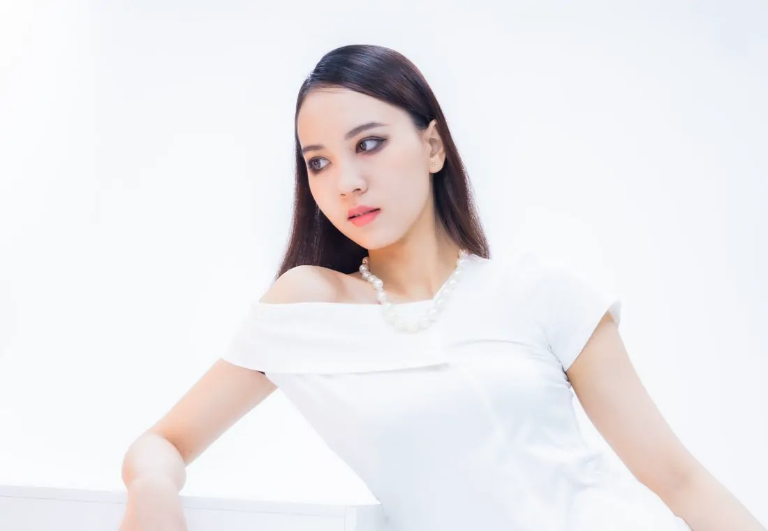 Mujer con vestido blanco y collar de perlas sobre fondo claro