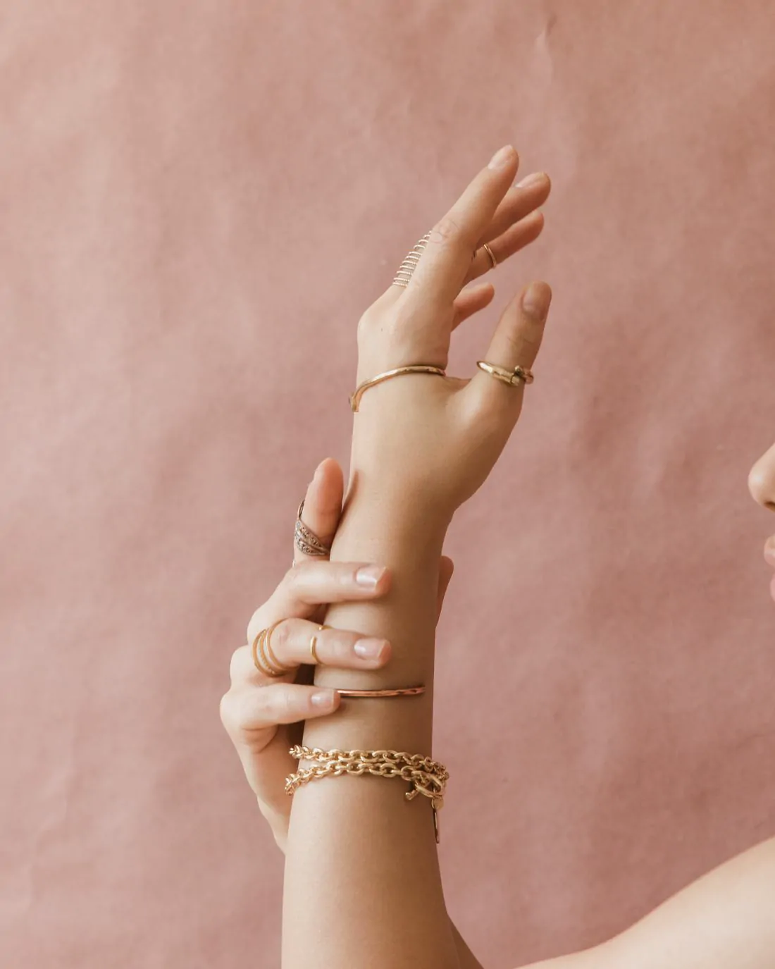 Muñeca con pulsera trenzada de oro sobre fondo rosa palo